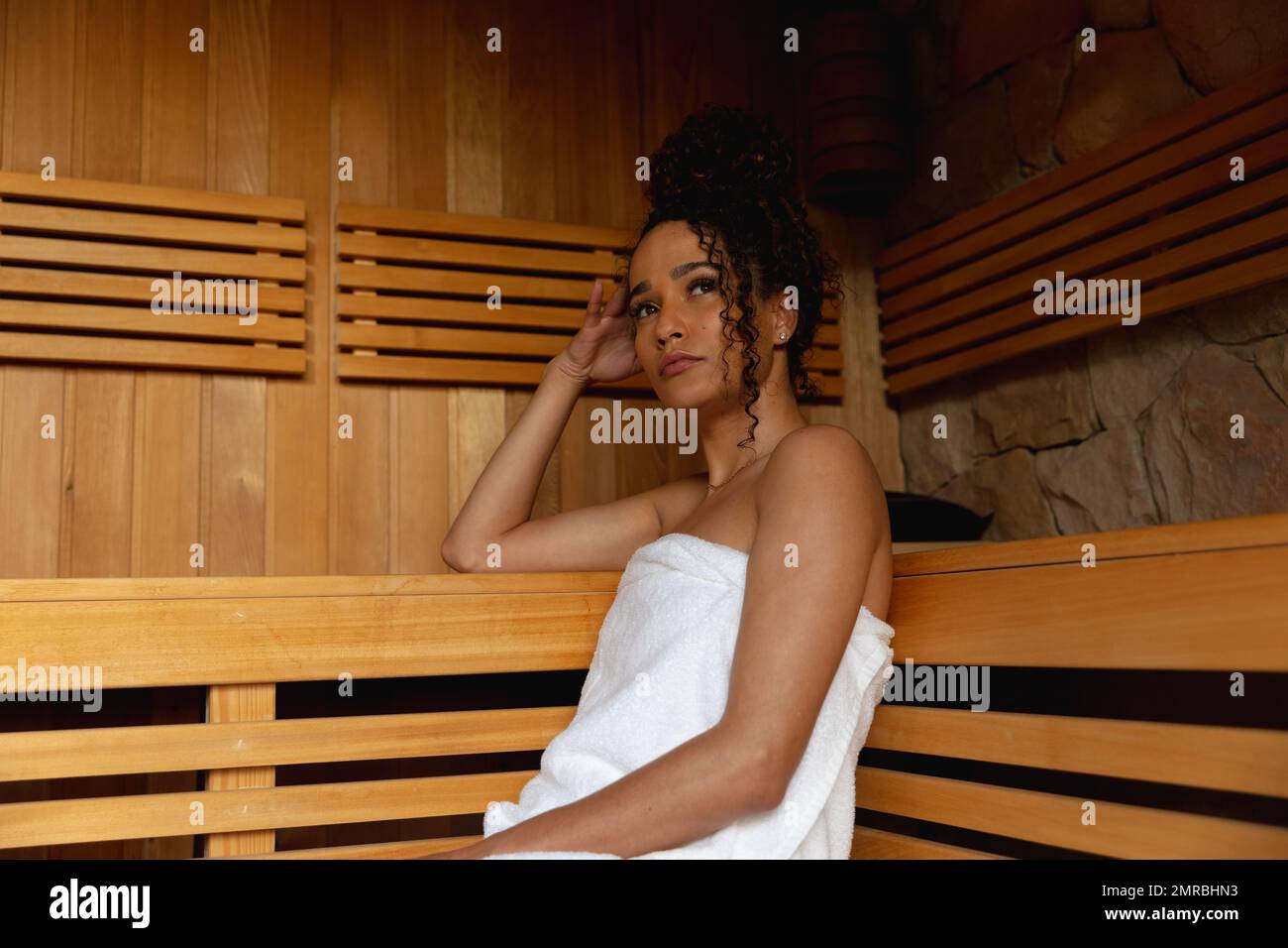 Femme biraciale attentionnés portant une serviette de détente sur le banc dans le sauna, salle de photocopie Banque D'Images