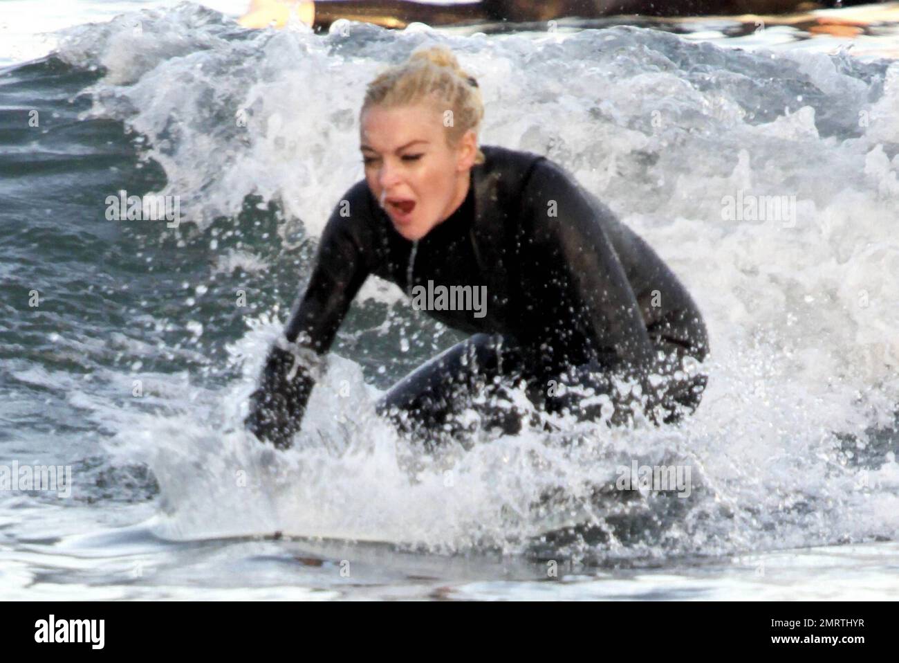 Lindsay Lohan tire quelques visages drôles tout en apprenant à surfer. Portant une combinaison noire, Lohan a tiré ses longs cheveux blonds dans un petit pain et a sauté dans les vagues avec une longue planche. Bien qu'il ait essuyé plusieurs fois, Lohan semblait passer un excellent moment. Malibu, Californie 16 août 2011. Banque D'Images
