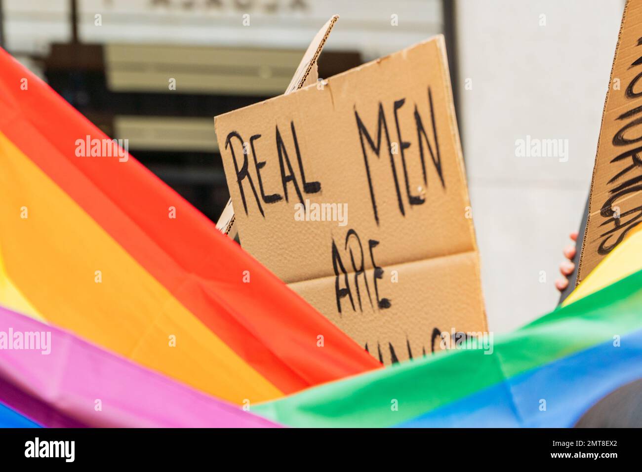 Jeune adulte gay avec drapeau lgbtq et soutien d'un message féministe écriteau sur une manifestation dans la rue Banque D'Images