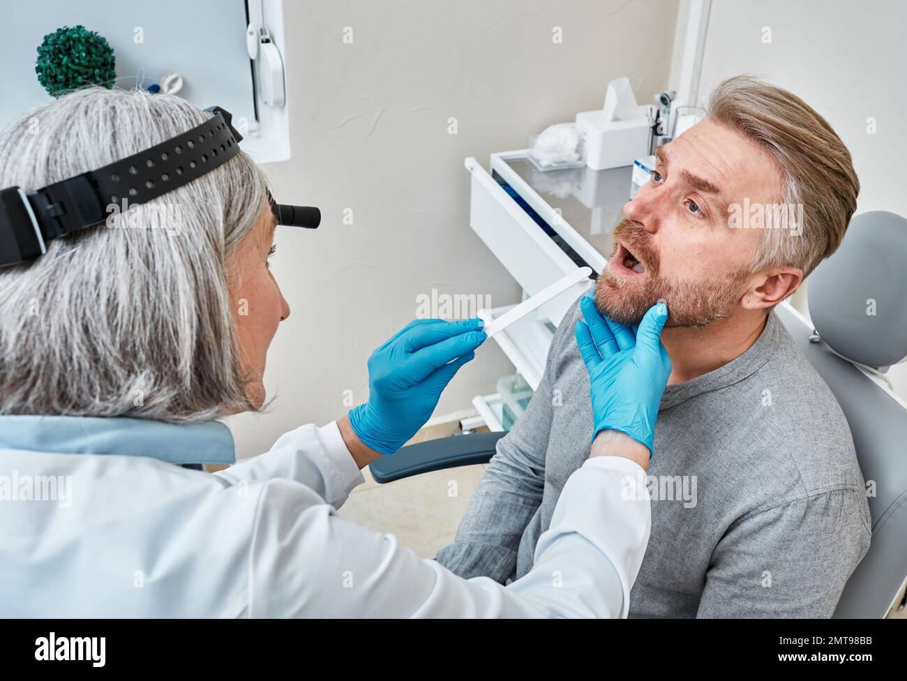 Un médecin expérimenté utilisant une spatule d'inspection examine la gorge d'un patient mâle au cours d'un examen médical. Consultation du médecin ORL, examen de la gorge Banque D'Images