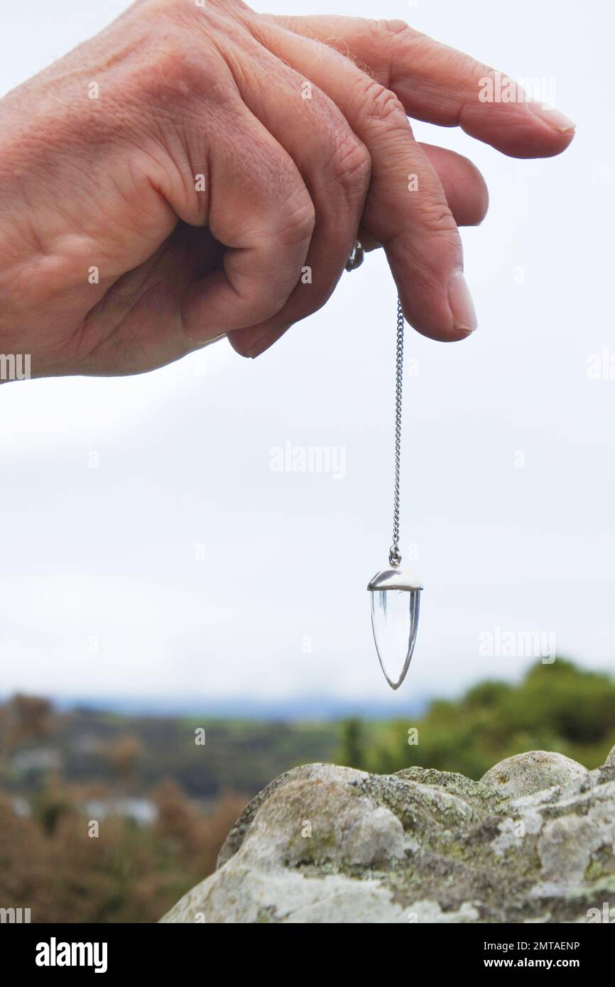 Main mâle utilisant un pendule de cristal qui danse sur une pierre debout - John Gollop Banque D'Images