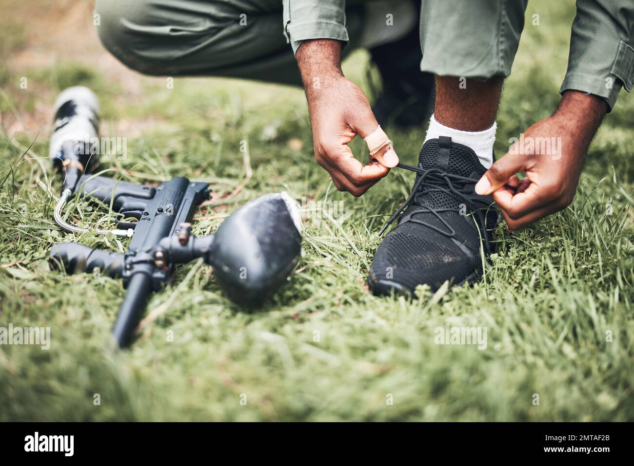 Paintball, pistolet et tireur ou homme prêt à se mettre à genoux pour un match de compétition ou de compétition dans la forêt. Joueur, athlète et personne nouant les lacets avec le jeu Banque D'Images