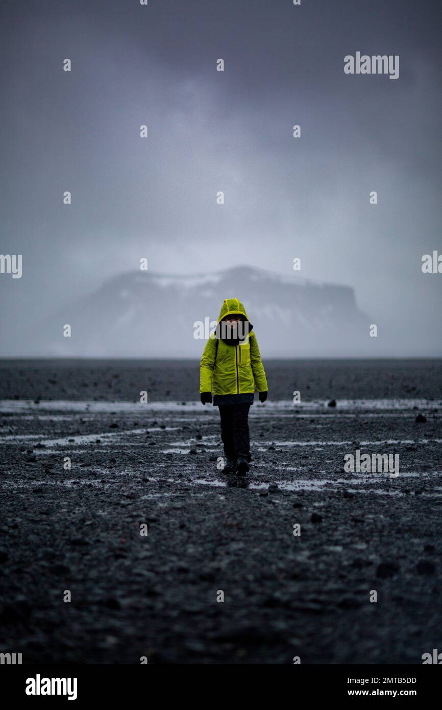 Fille avec une veste jaune sur le chemin de l'épave d'avion de Solheimasandur DC-3 avec le Mont Pétursey en arrière-plan, Sólheimasandur, Islande Banque D'Images