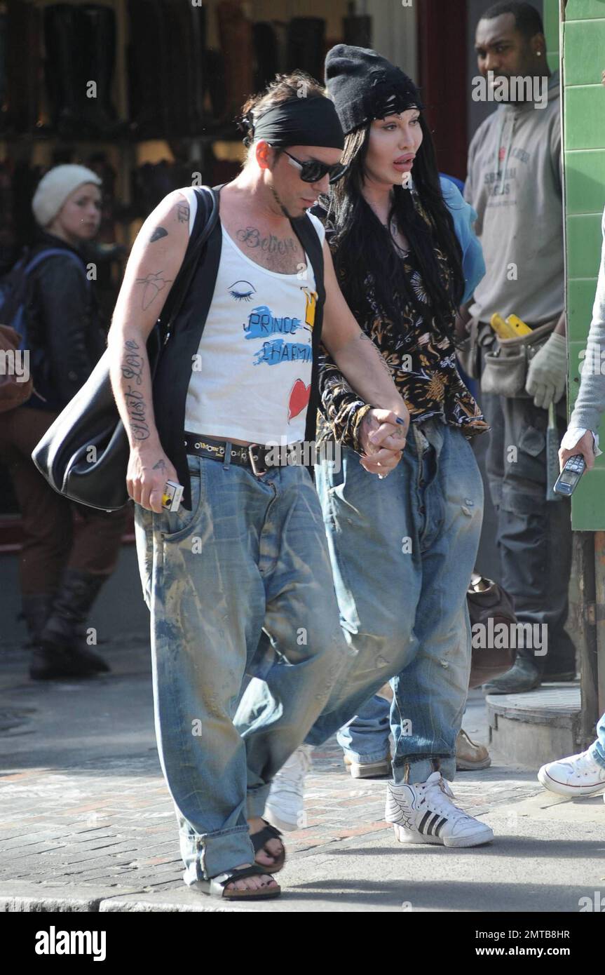 Reality TV et Pete Burns (You Spin Me Round), la star pop des années 80, fait du shopping à Soho avec un petit ami et montre simultanément les effets choquants de plusieurs chirurgies du visage en plastique. Burns et son petit ami, qui semble avoir juste eu une chirurgie faite sur son visage bandé, portent des jeans aussi aggeux et tiennent les mains pendant qu'ils marchent. Londres, Royaume-Uni. 10/07/10. Banque D'Images