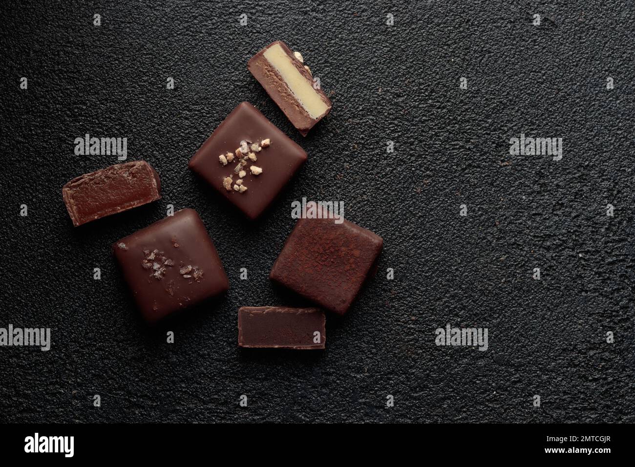 Bonbons au chocolat faits à la main et morceaux de bonbons coupés avec praline et truffe sur fond noir avec bannière horizontale d'espace de copie Banque D'Images