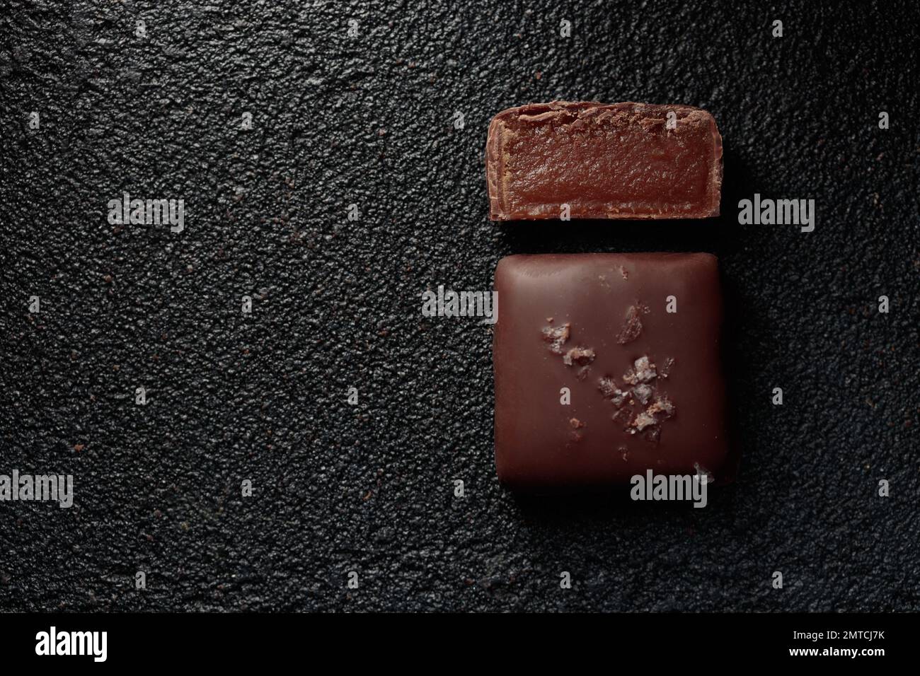 Bonbons au chocolat faits à la main et morceau de bonbons coupés au caramel sur fond noir avec photo horizontale d'espace de copie Banque D'Images