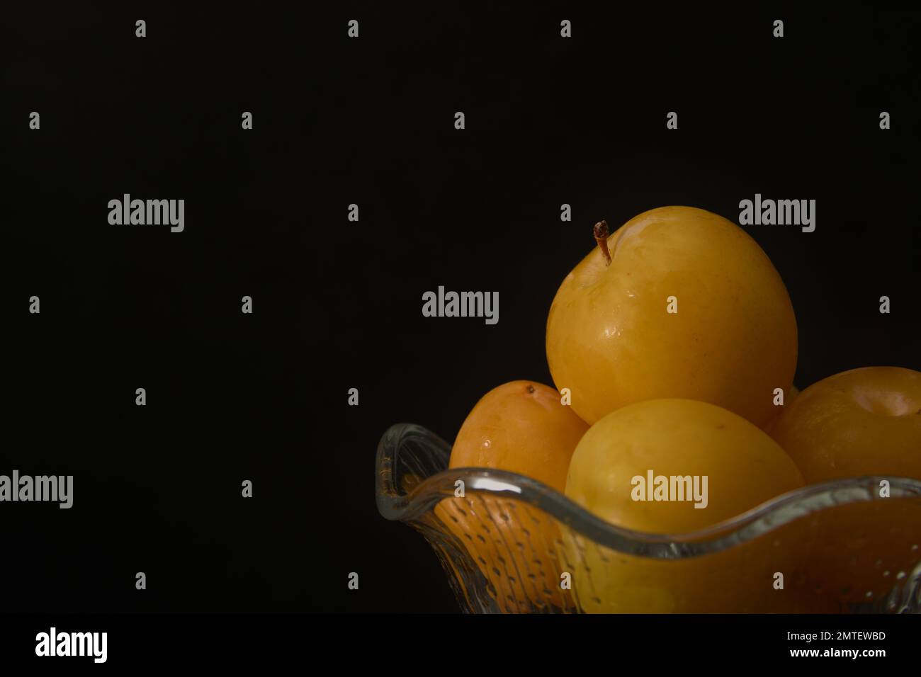 Gros plan d'un bol en verre contenant des prunes jaunes mûres fraîches avec un fond noir et un espace de copie Banque D'Images