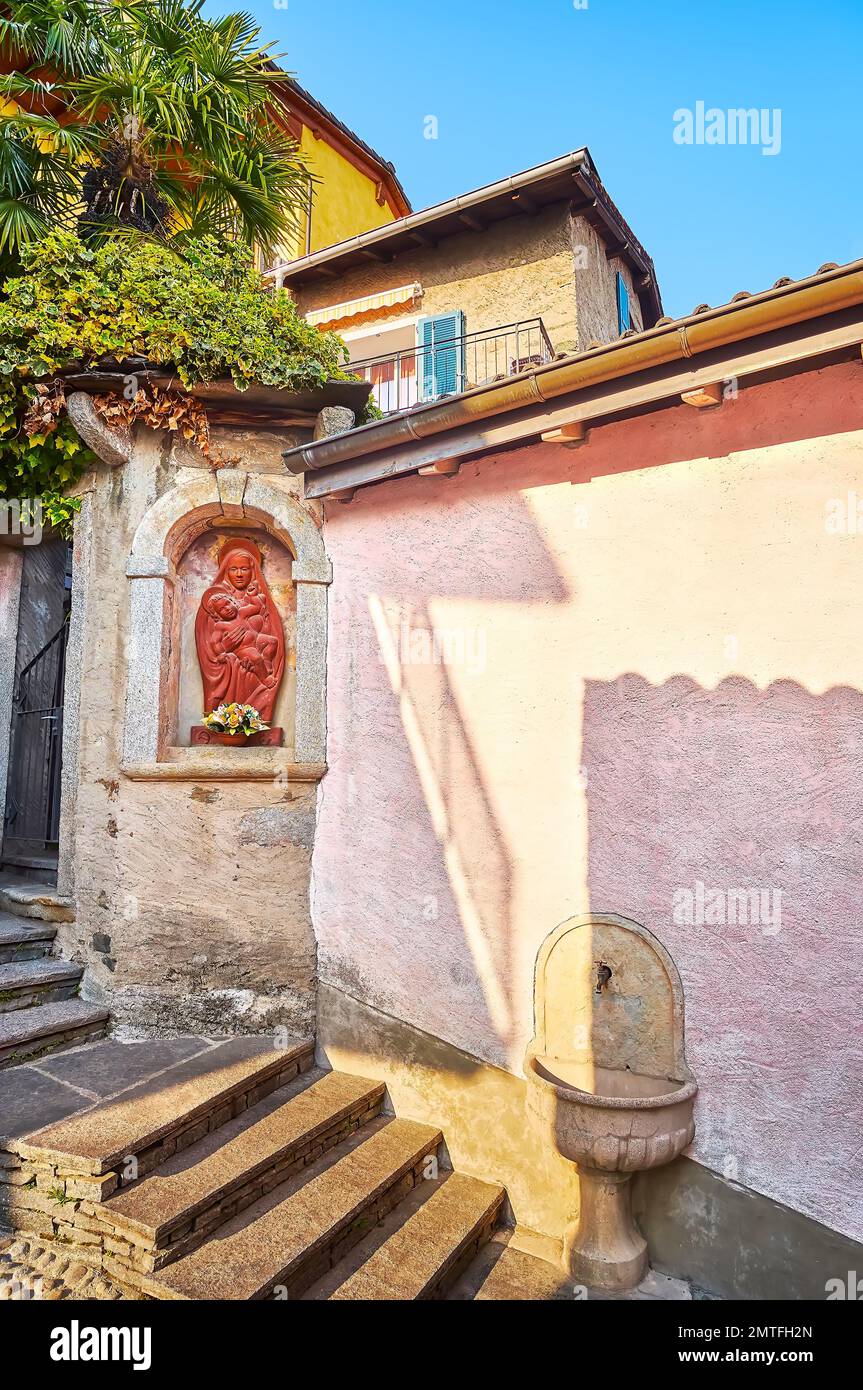 La petite chapelle avec une sculpture murale de la Vierge Marie et une police d'eau sainte en pierre dans la vieille rue de Ronco sopra Ascona, Tessin, Suisse Banque D'Images
