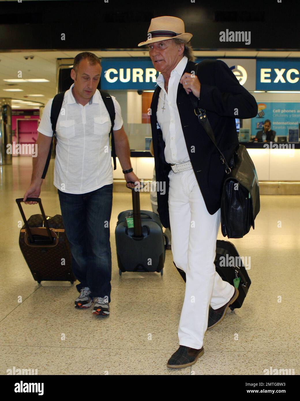 À la recherche de la capule dans une tenue blanche, veste noire et fedora, Rod Stewart, avec sa famille à la remorque, arrive à l'aéroport international de Miami. Stewart a mis son bagage à main alors que l'épouse Penny Lancaster poussait le fils Aiden dans une poussette avec le fils Alistair à proximité. Miami, Floride. 11th janvier 2012. Banque D'Images