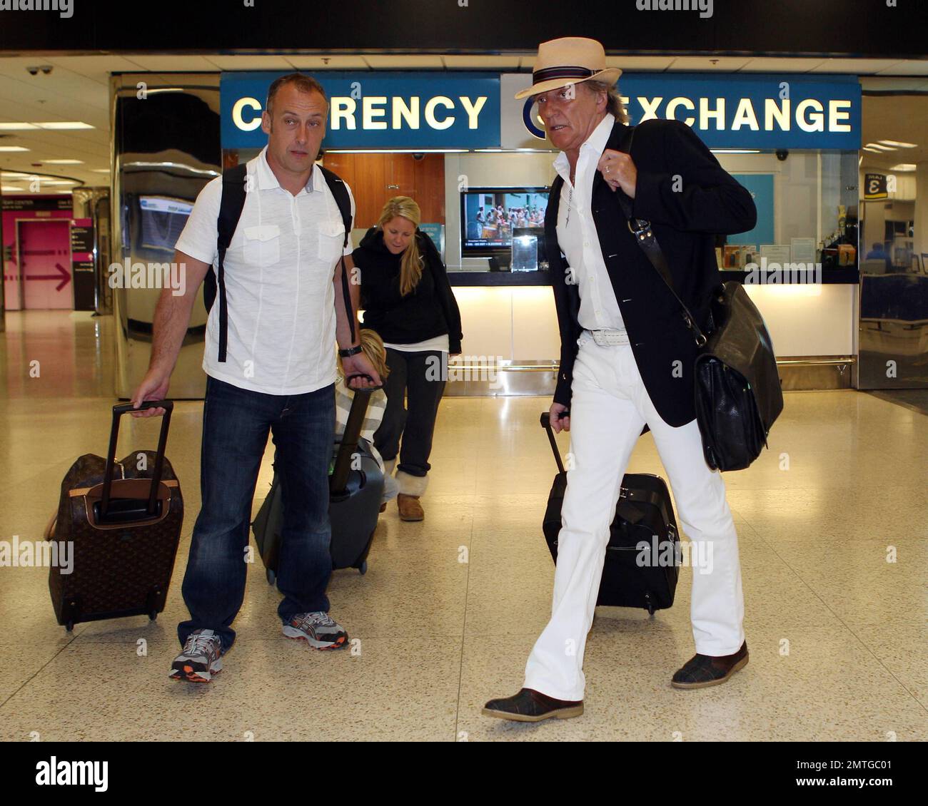 À la recherche de la capule dans une tenue blanche, veste noire et fedora, Rod Stewart, avec sa famille à la remorque, arrive à l'aéroport international de Miami. Stewart a mis son bagage à main alors que l'épouse Penny Lancaster poussait le fils Aiden dans une poussette avec le fils Alistair à proximité. Miami, Floride. 11th janvier 2012. Banque D'Images