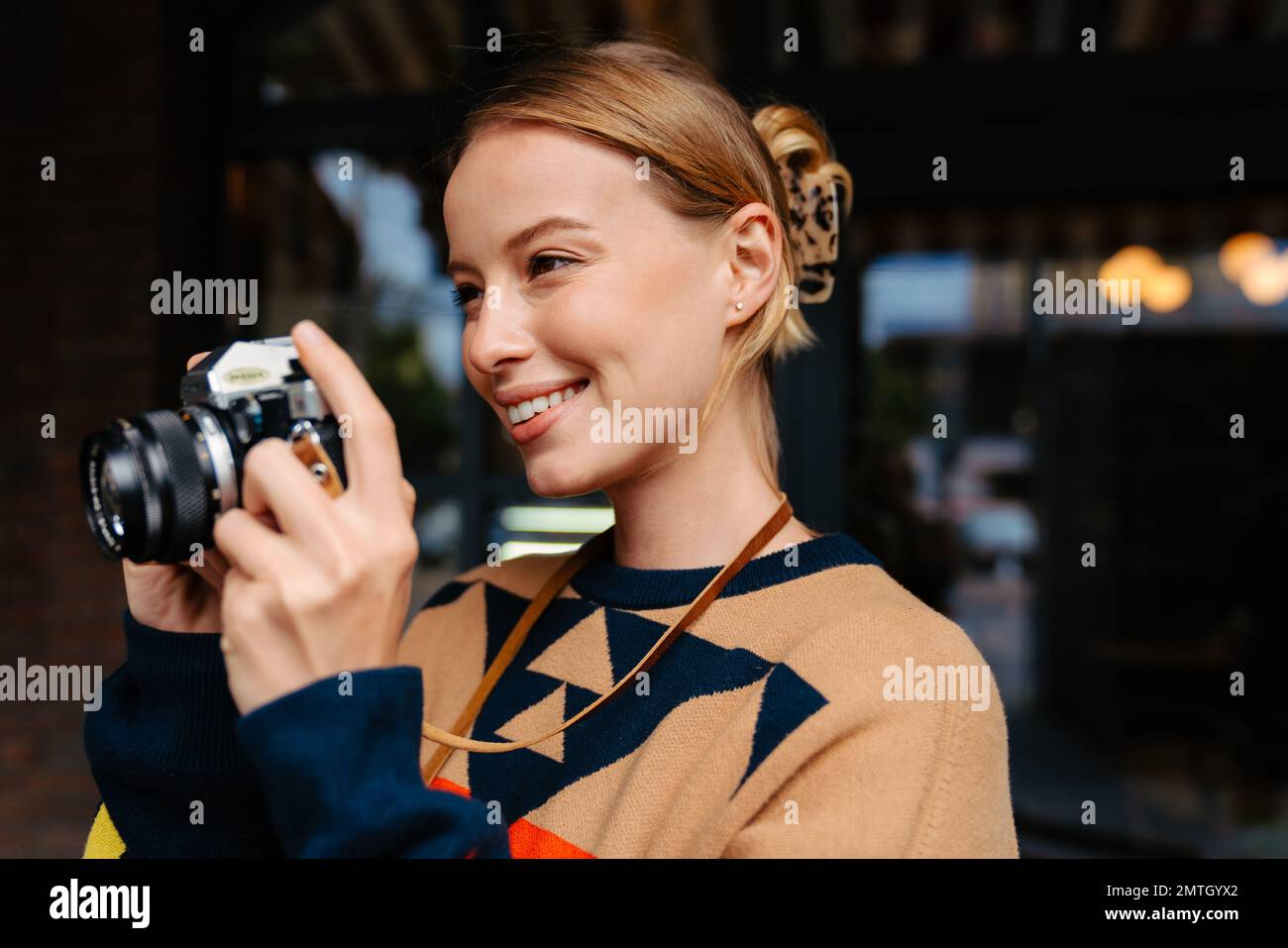 Joyeuse femme blonde photographe en chandail prendre des photos sur un appareil photo rétro tout en marchant à l'extérieur Banque D'Images