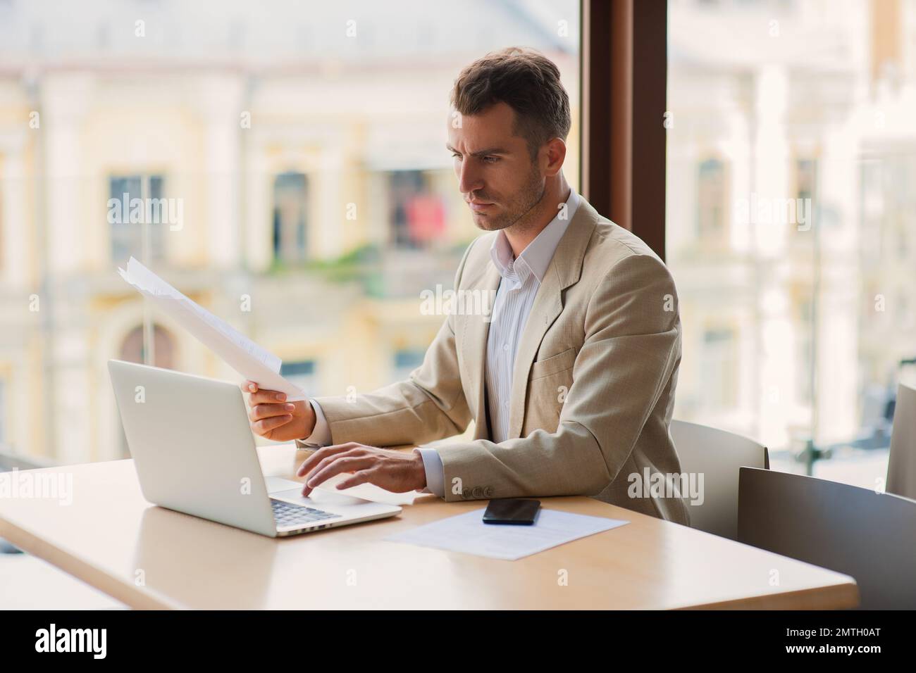 Un homme élégant homme d'affaires commerçant confiant travaillant sur la bourse un café de boire dans un petit café, tout en lisant un journal et de travail ordinateur portable Banque D'Images