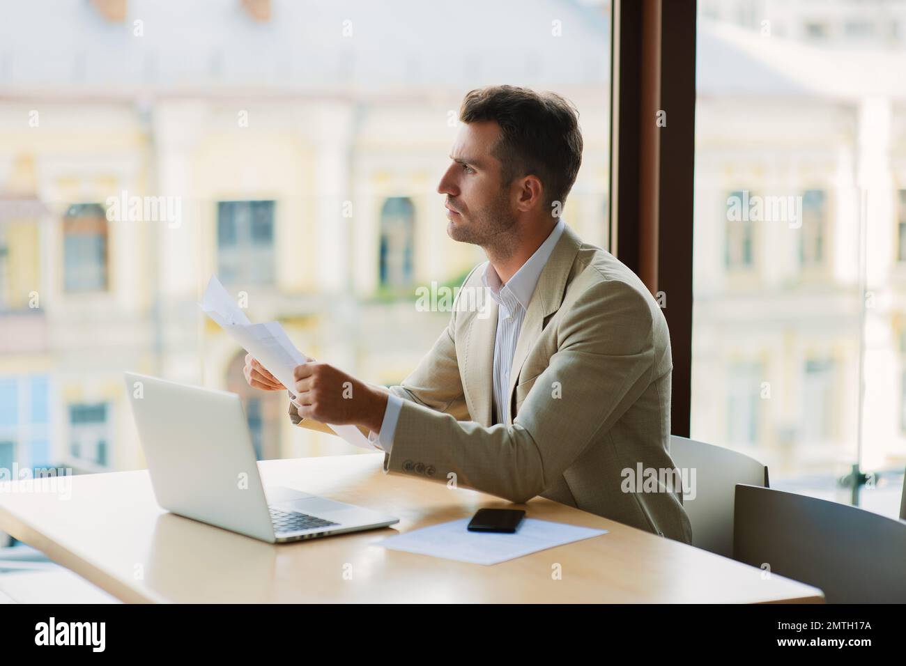 Un homme élégant homme d'affaires commerçant confiant travaillant sur la bourse un café de boire dans un petit café, tout en lisant un journal et de travail ordinateur portable Banque D'Images