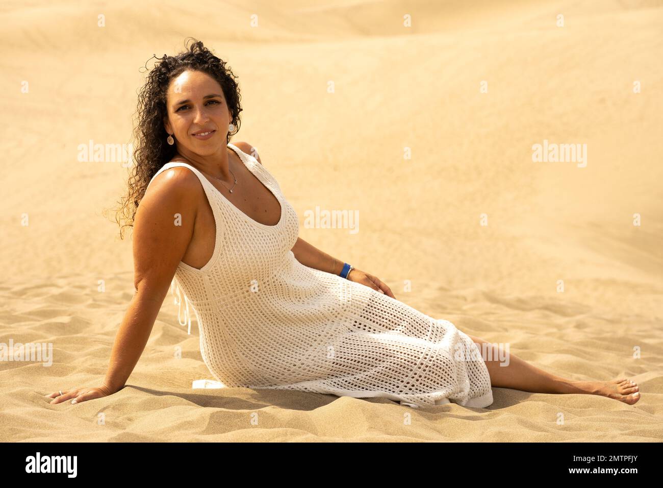 Une femme caucasienne portant une robe blanche assise dans le désert de Maspalomas à Gran Canaria, en Espagne Banque D'Images