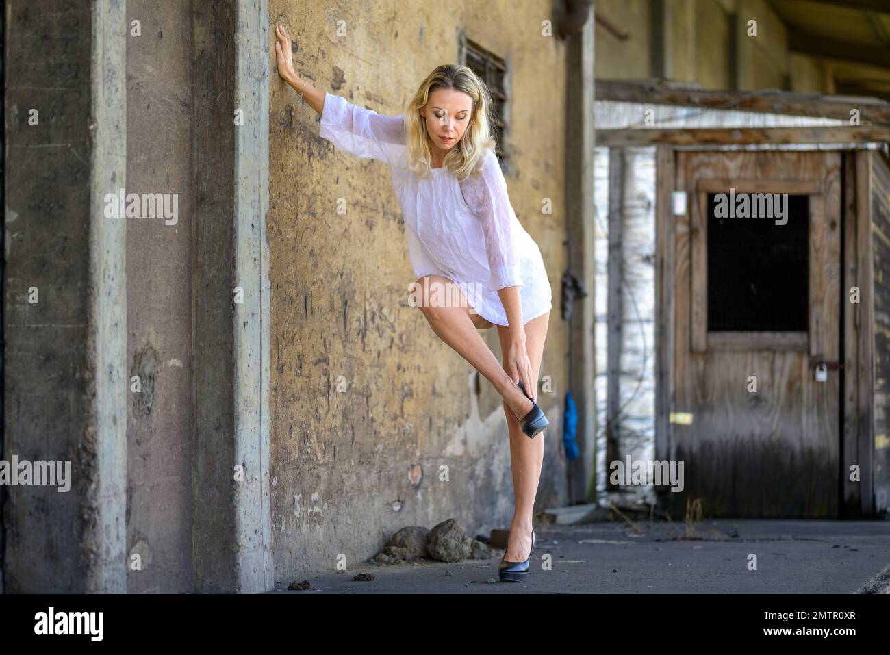 Blonde d'âge moyen belle femme portant une robe courte blanche penchée contre un mur mettant ses chaussures Banque D'Images