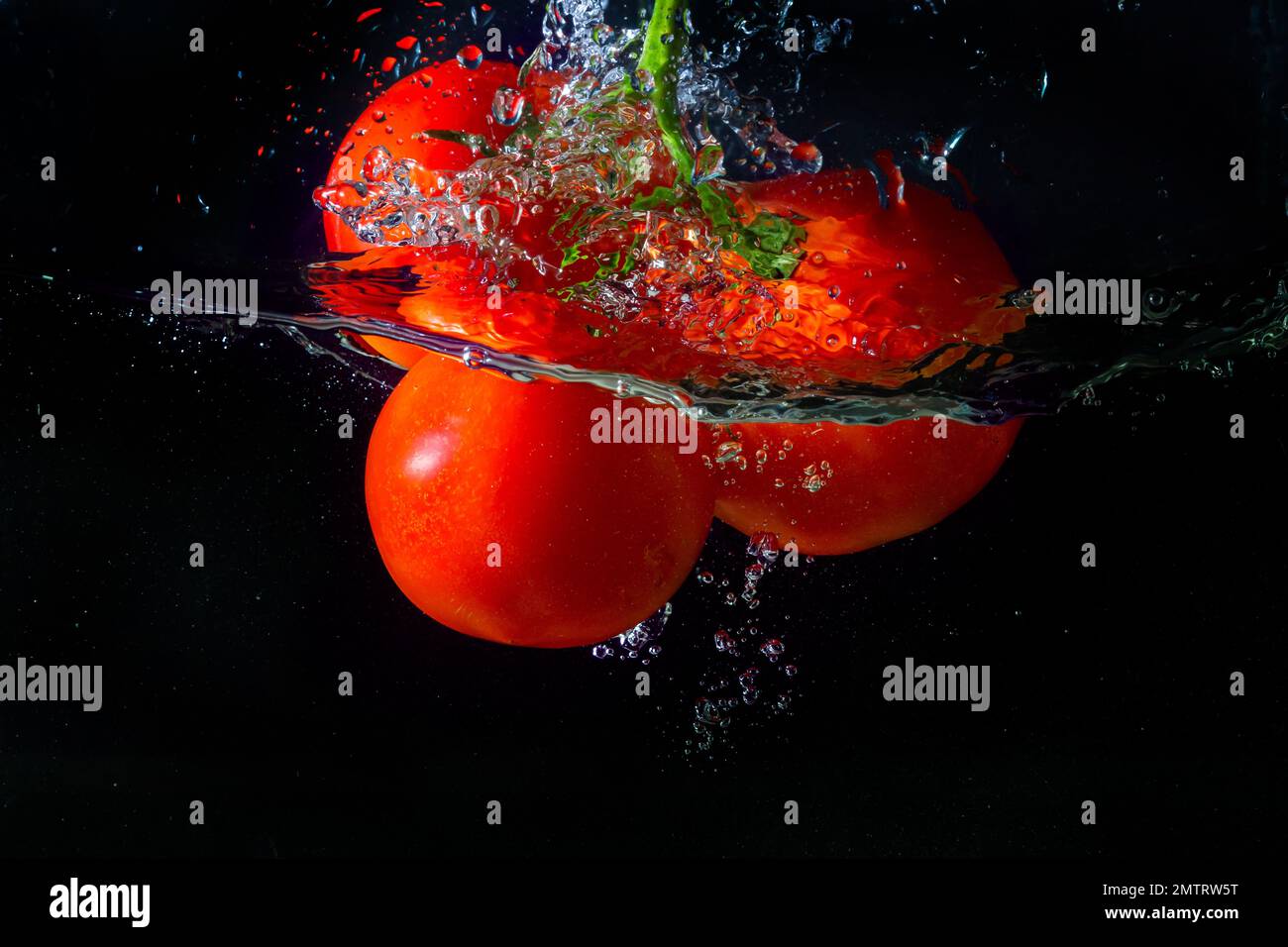 Tomate rouge fraîche tombant dans l'eau avec des éclaboussures d'eau et des bulles d'air isolées sur fond noir. Banque D'Images