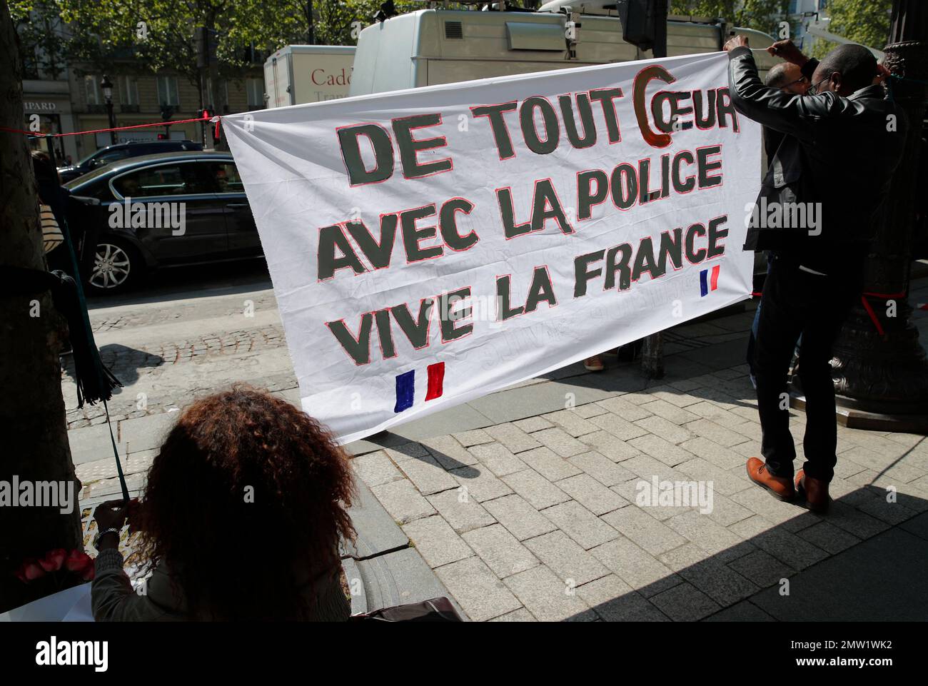 Three people set up a banner reading "Our hearts with the police, Long live France" at the place where a police officer was killed Thursday on the Champs Elysees boulevard, Friday, April 21, 2017 in Paris. The Champs-Elysees gunman who shot and killed a police officer just days before France's presidential election was detained in February for threatening police but then freed, two officials told The Associated Press on Friday. (AP Photo/Christophe Ena) Banque D'Images