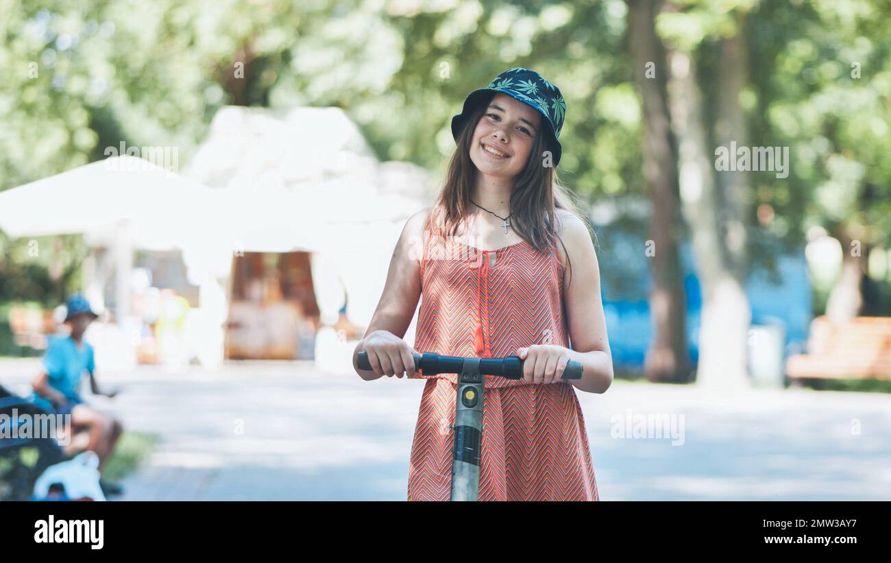 Portrait d'une fille sur un scooter électrique posé dans un parc en été. Banque D'Images