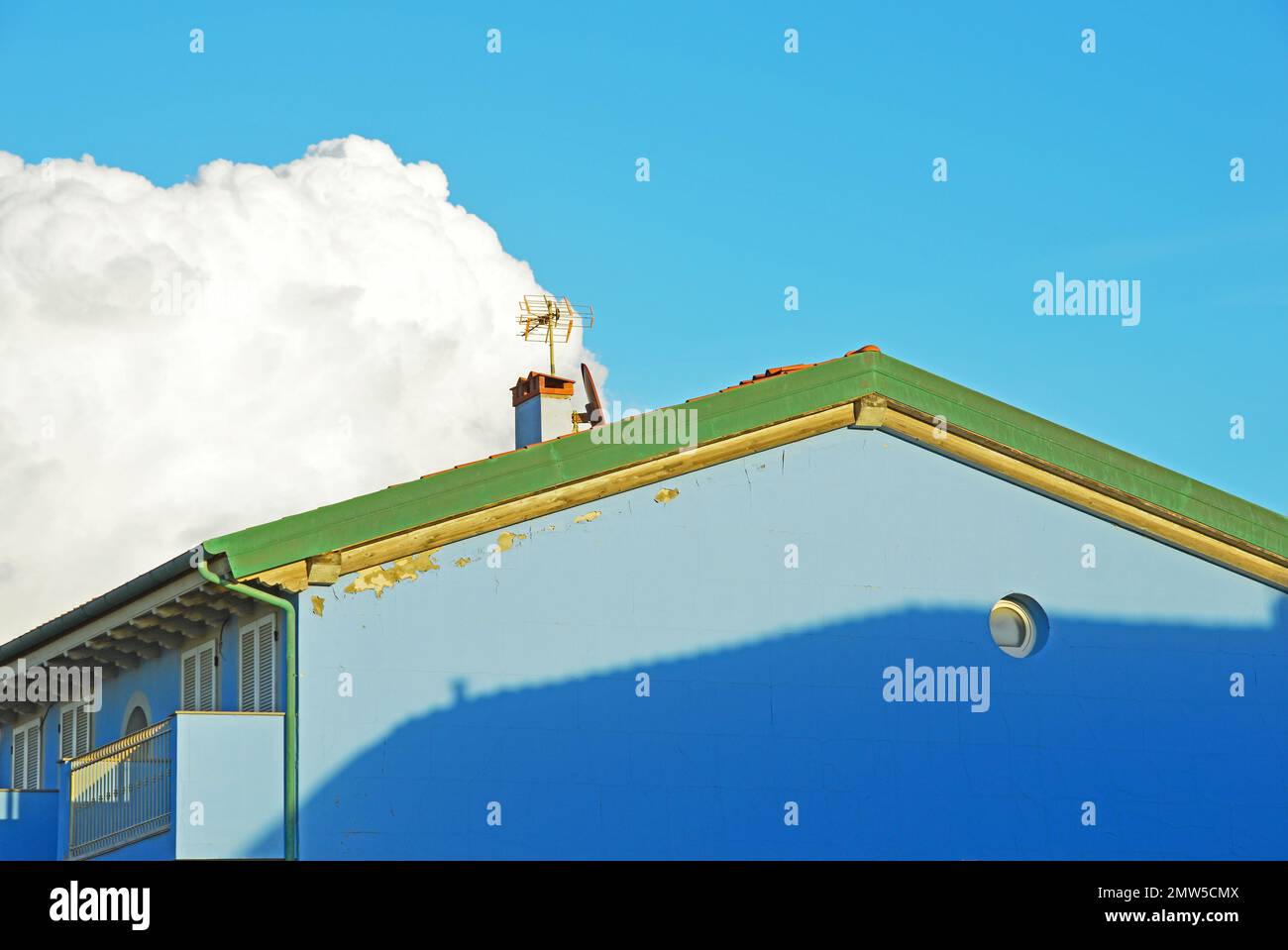 Un fragment de la façade d'une maison bleue sur le fond du ciel avec un grand nuage de cirrus Banque D'Images