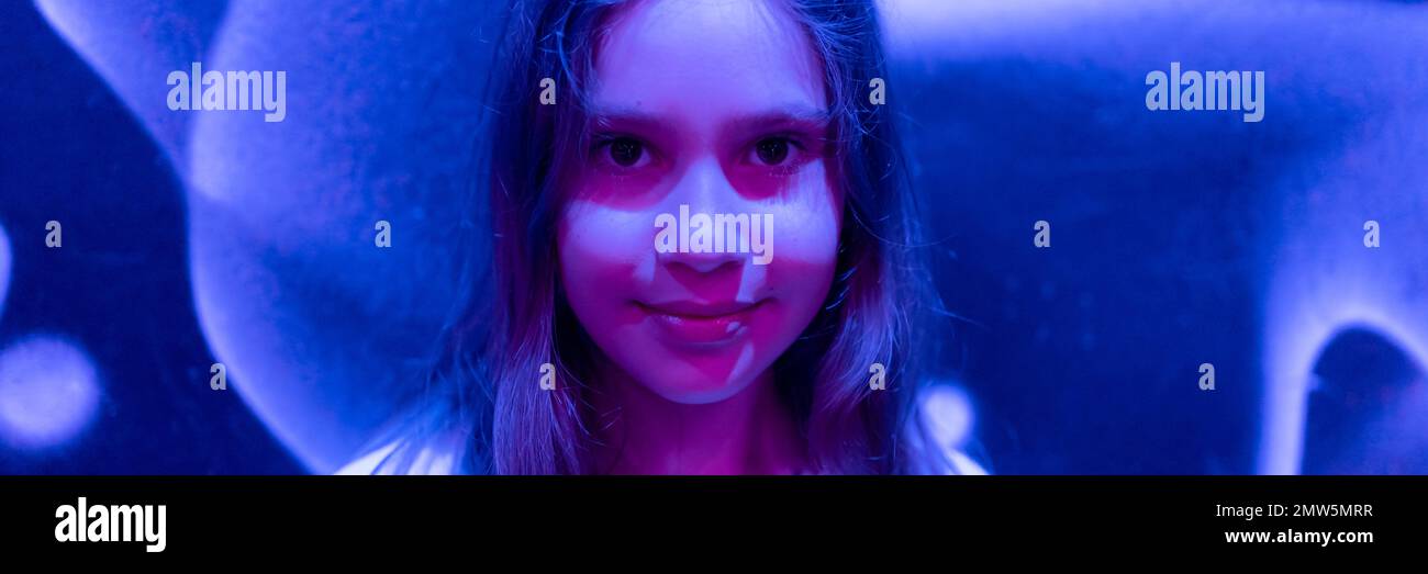 portrait visage mignon bonne candide caucasien préteen jeune fille de neuf ans dans le studio illuminé par lumière bleue violet néon. bannière Banque D'Images