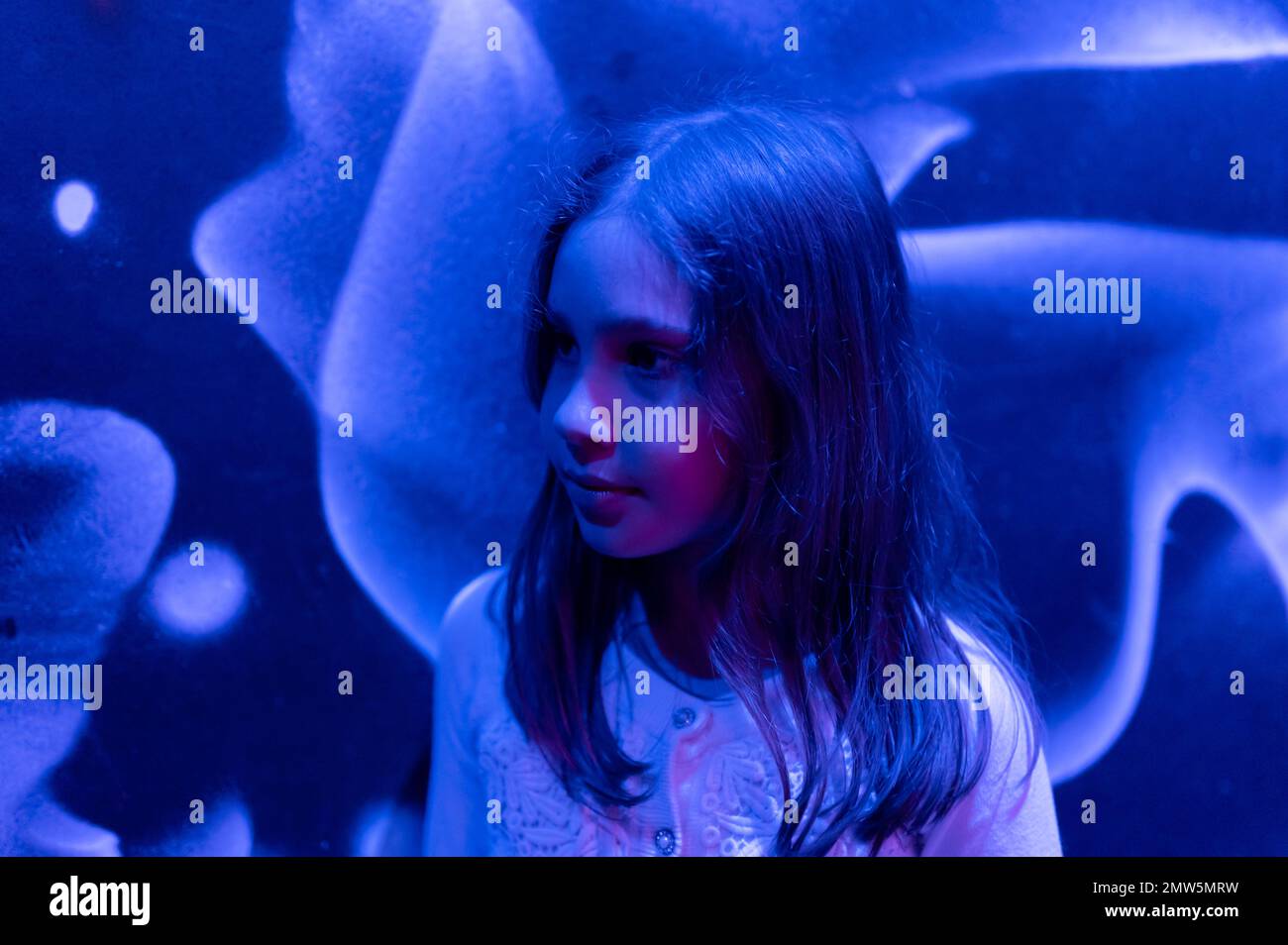 portrait visage mignon heureux candié caucasien pré adolescent neuf ans petite fille dans le profil dans le studio éclairé par lumière bleue violet néon Banque D'Images