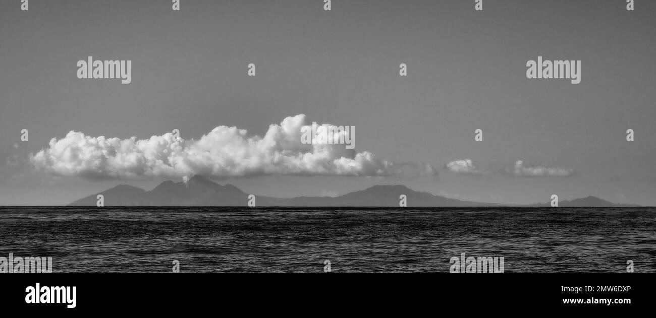 Une vue en noir et blanc de la silhouette de l'île de Montserrat avec des nuages bas au-dessus du volcan en éruption dans un ciel autrement clair Banque D'Images
