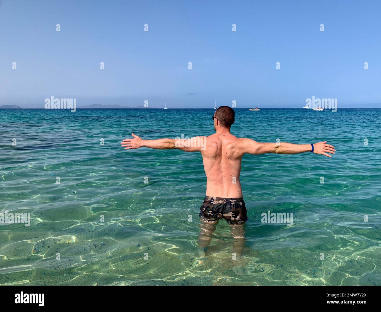 Homme aux bras ouverts comme signe de liberté. Bord de mer, immergé dans les eaux turquoise de la mer de Lanzarote. Banque D'Images