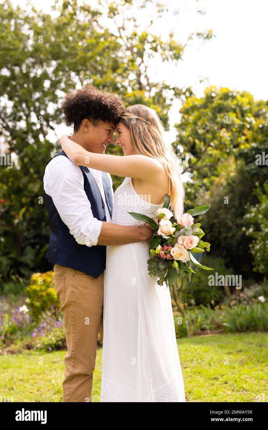 Vertical de la mariée et marié heureux et divers avec bouquet embrassant au mariage dans le jardin Banque D'Images