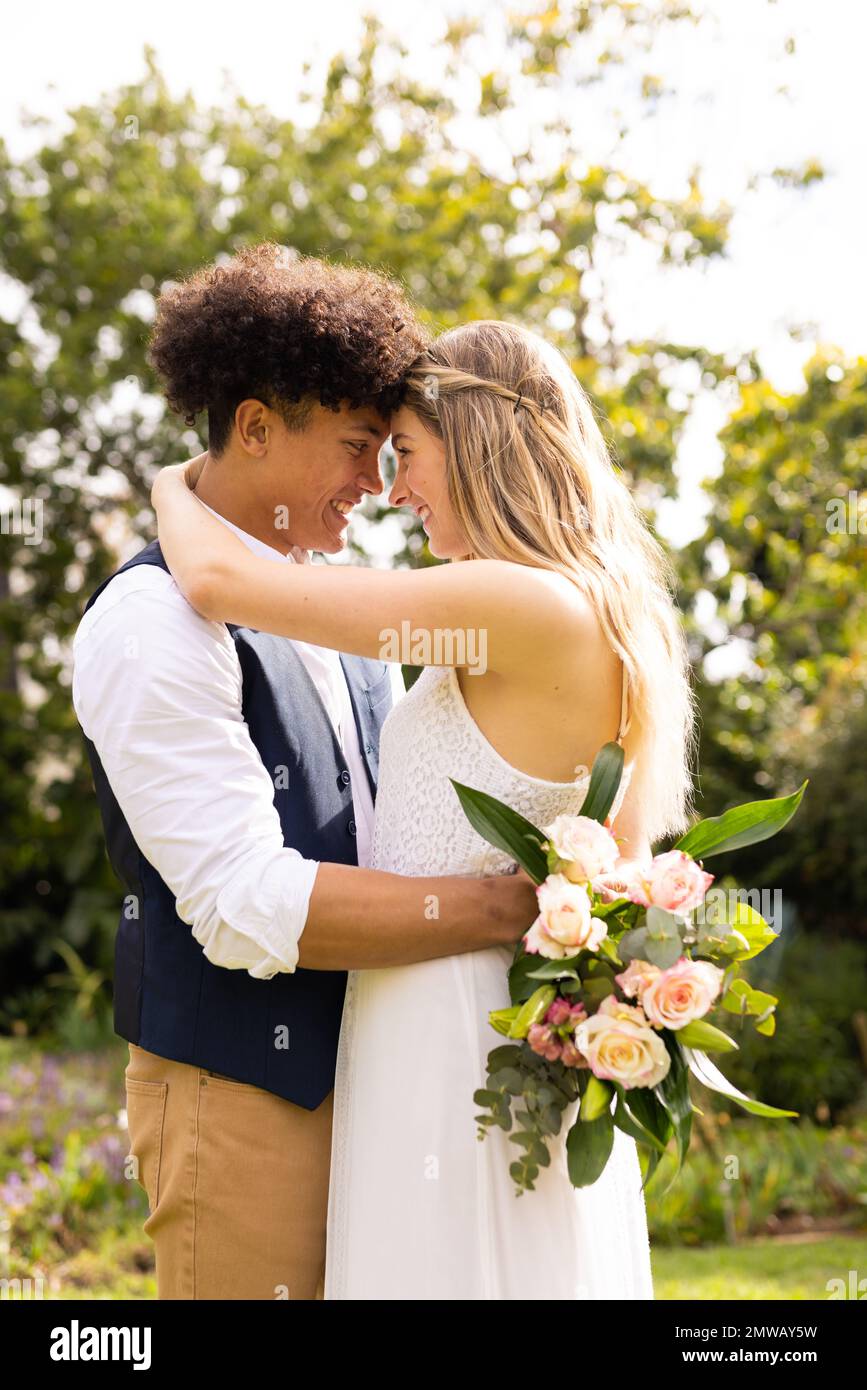 Vertical de la mariée et marié heureux et divers avec bouquet embrassant au mariage dans le jardin Banque D'Images