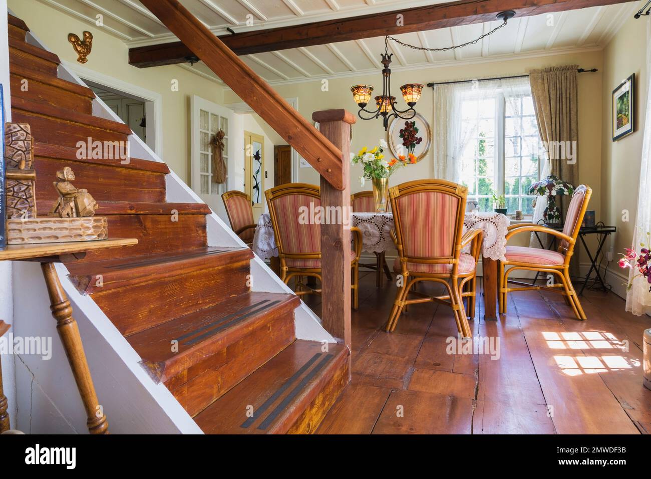 Escalier en bois menant à l'étage supérieur et à la salle à manger avec fauteuils en rotin et table en bois à l'intérieur de l'ancienne maison reconstruite de style Canadiana de 1886. Banque D'Images