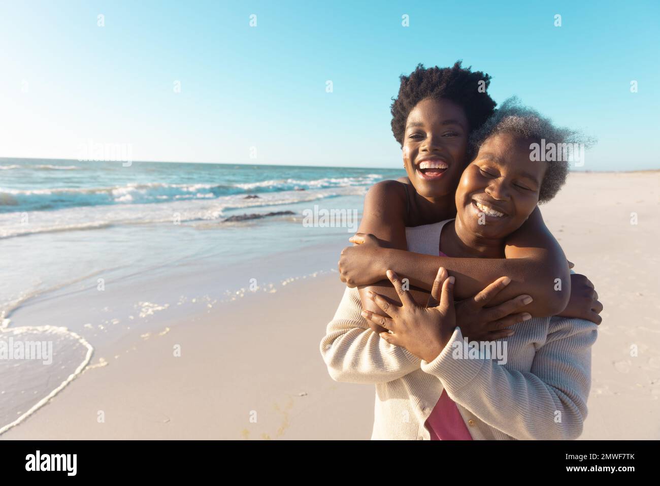 Bonne jeune femme afro-américaine riant et embrassant la mère tout en se tenant contre la mer et le ciel Banque D'Images