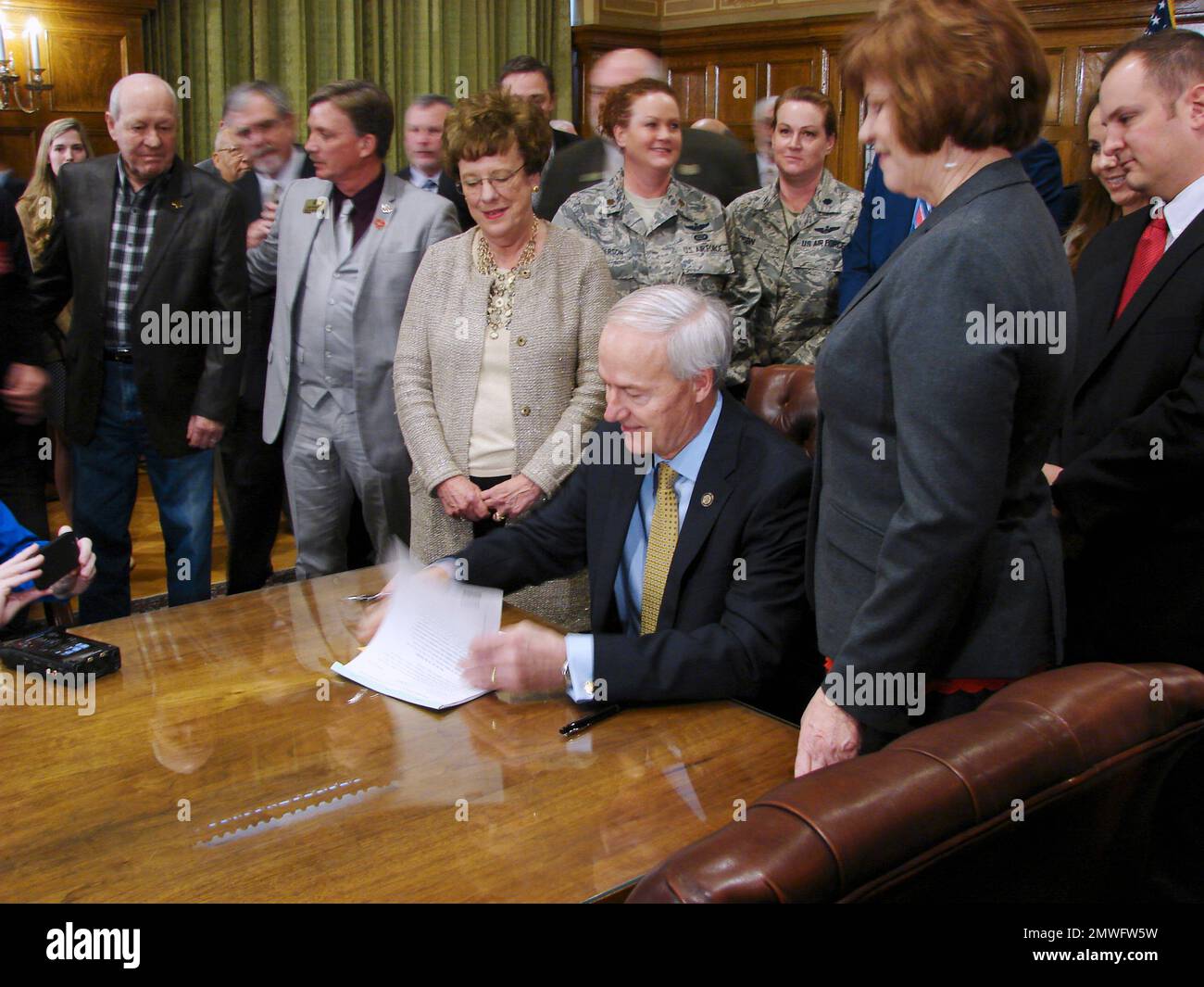Arkansas Gov. Asa Hutchinson signs a bill in his Capitol conference room in Little Rock on Tuesday, Feb. 7, 2017, to cut income taxes on military retirement benefits as Sen. Jane English, center, looks on. The tax cut is intended to help promote economic development by attracting retirees to the state. Arkansas will raise taxes on unemployment benefits, soda, candy and digital downloads to pay for it. (AP Photo/Kelly P. Kissel) Banque D'Images