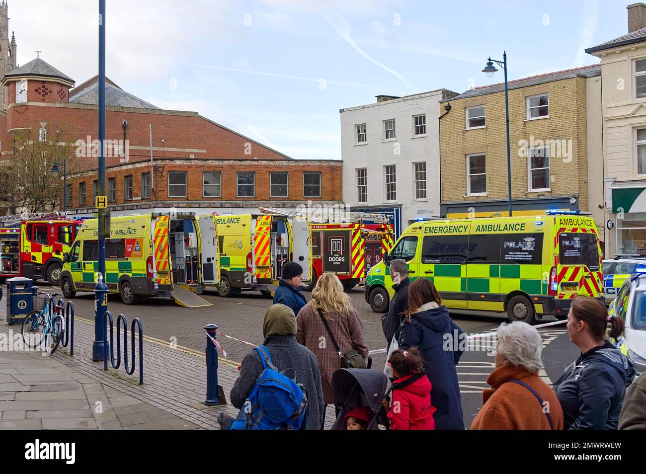 Les gens regardent tandis que les ambulances et les moteurs d'incendie assistent à une scène après qu'une voiture s'est écrasée par une fenêtre de magasin de charité dans le quartier commerçant Banque D'Images