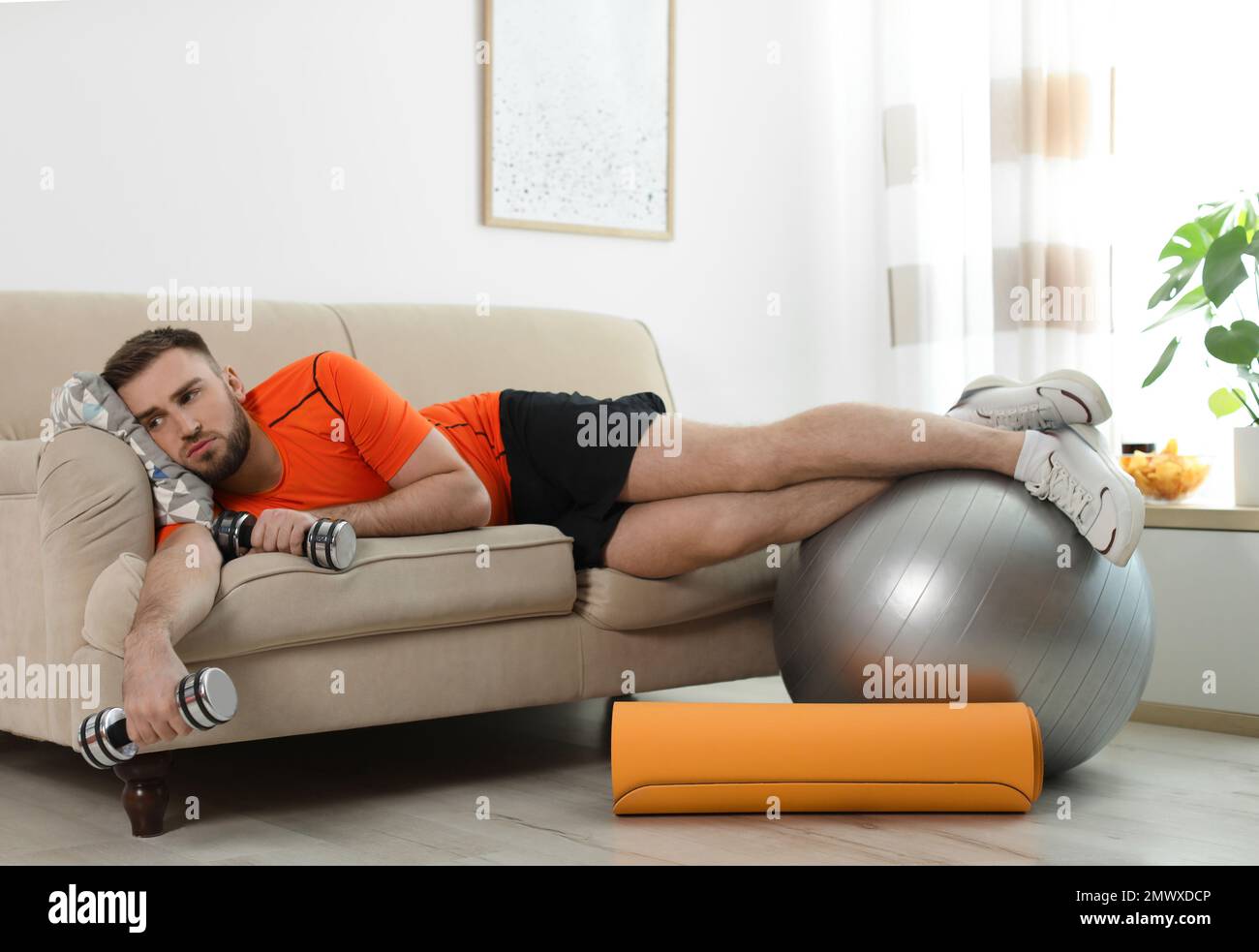 Jeune homme paresseux avec équipement de sport sur le canapé à la maison  Photo Stock - Alamy