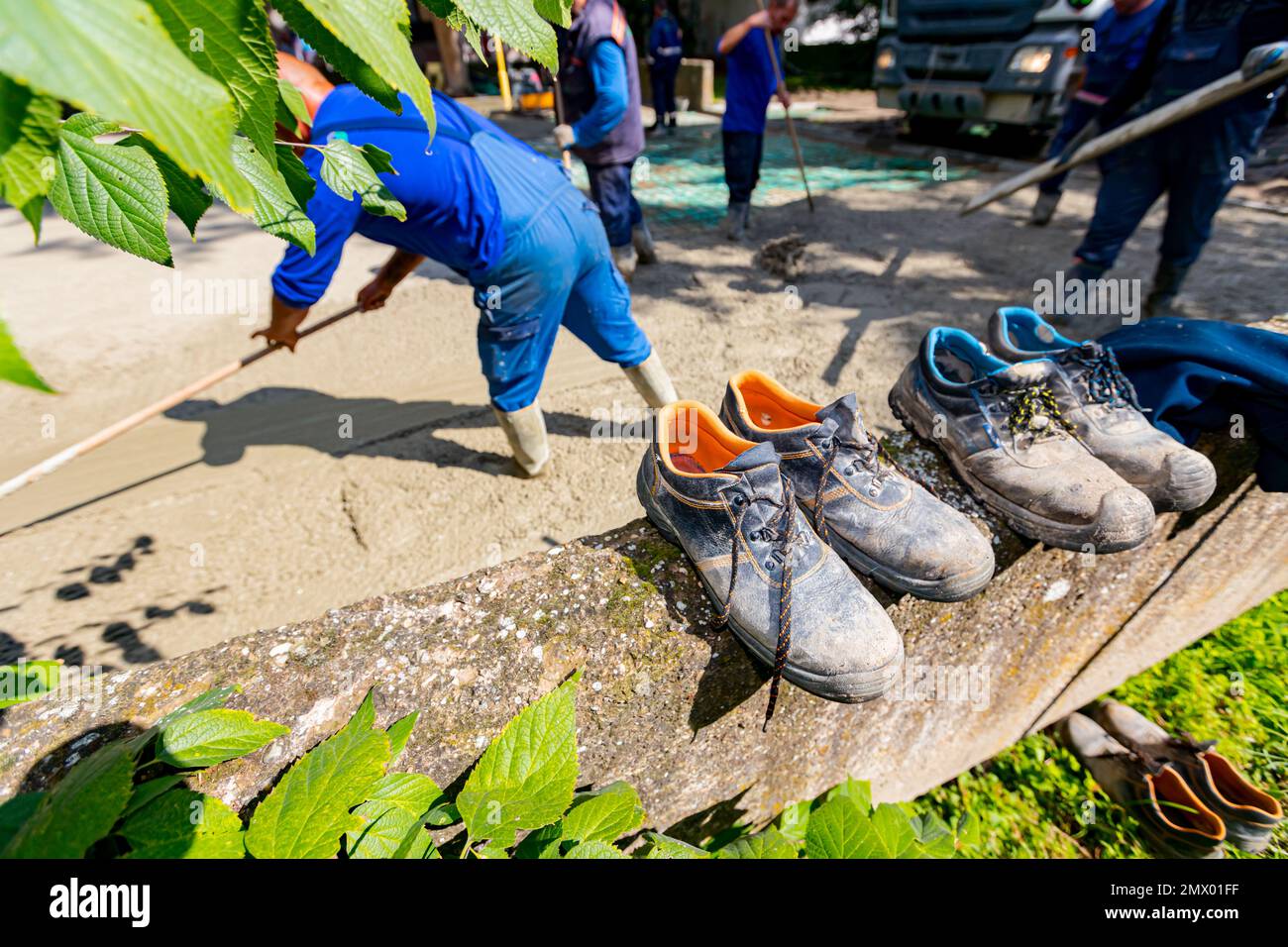 Vieilles chaussures de sécurité usées doublées, placées sur un petit mur  près du chantier de construction, car les ouvriers des bottes déversent du  béton et utilisent le râteau pour épandre, mettre à
