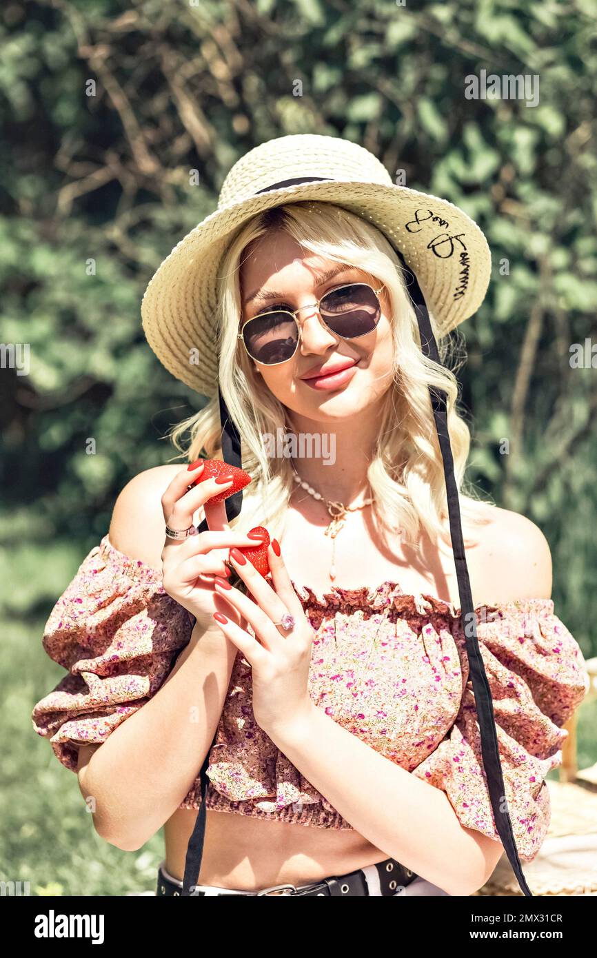 Photo d'une charmante jolie petite dame blonde qui tient une fraise dans sa main. Activités de plein air, pique-nique d'été. Banque D'Images