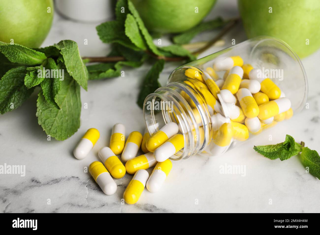 Bouteille avec des pilules de vitamines, des pommes et de la menthe sur une table en marbre blanc Banque D'Images