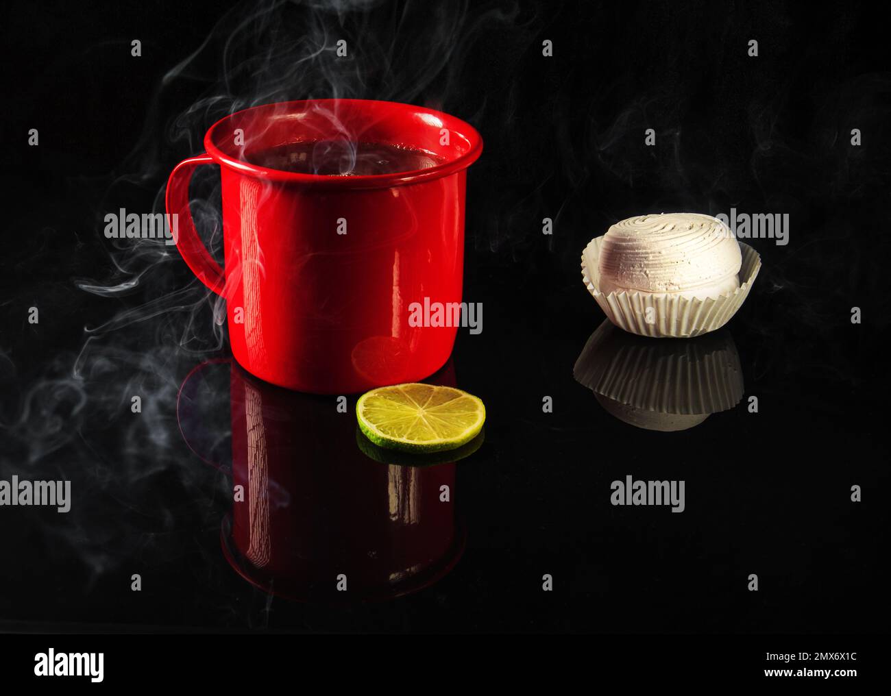 Tasse rouge avec thé chaud et guimauves blanches sur miroir noir. Banque D'Images