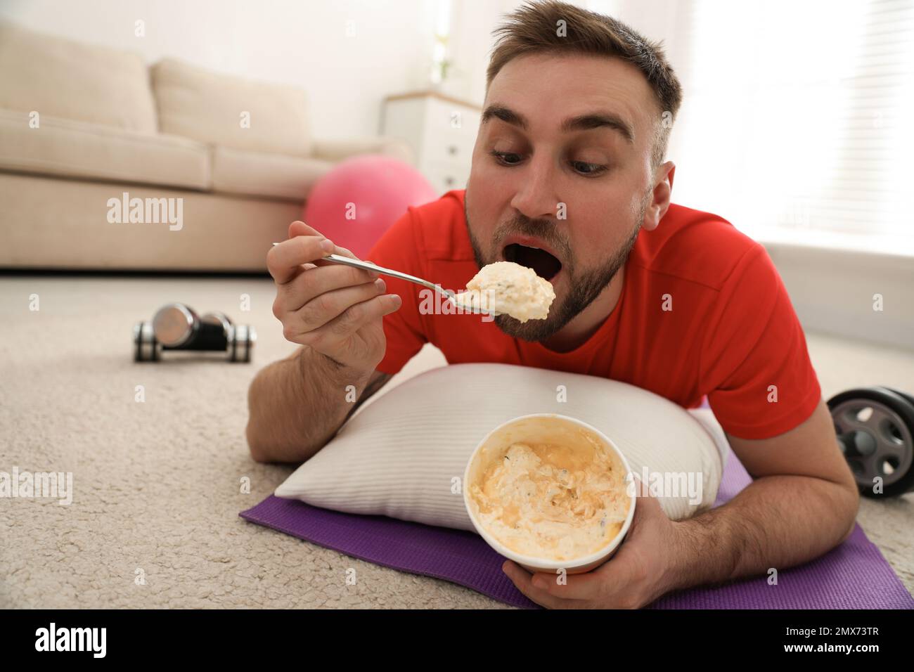 Un jeune homme paresseux qui mange de la crème glacée au lieu de s'entraîner à la maison Banque D'Images