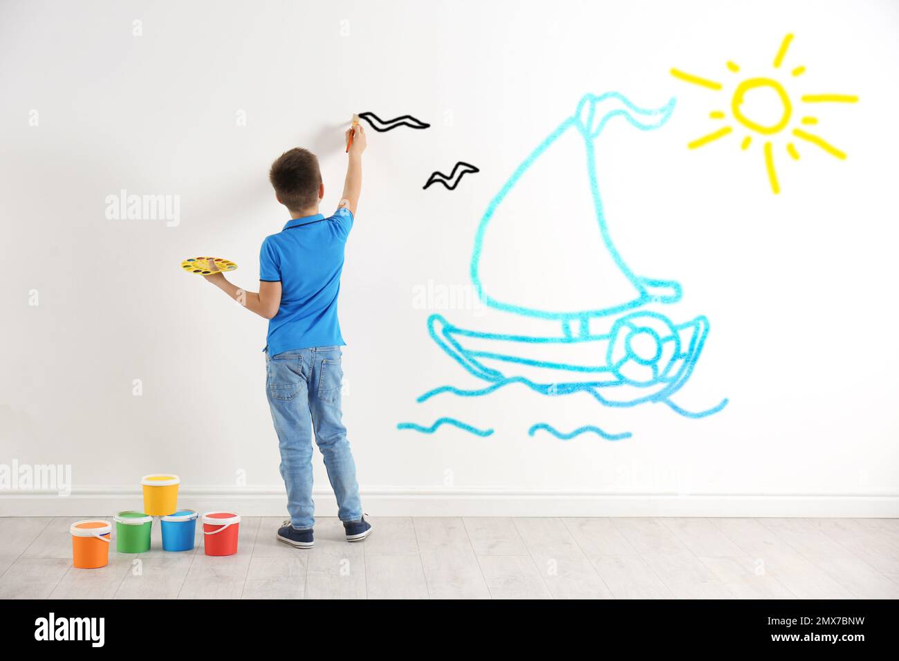 Un petit enfant dessine un bateau en mer sur un mur blanc à l'intérieur Banque D'Images