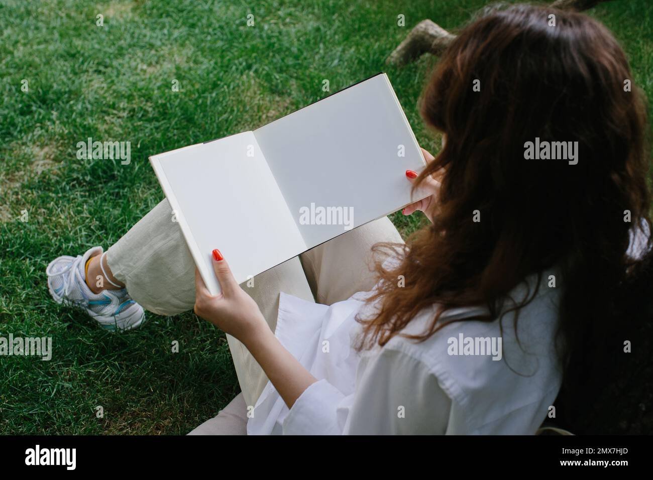 Maquette d'un magazine ou d'un livre. La fille se détend sur la pelouse dans la cour du café, lit un livre. Banque D'Images