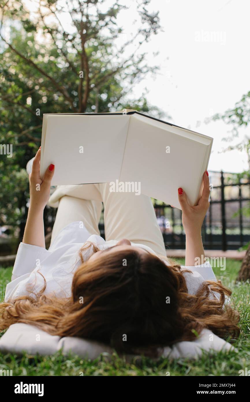 Maquette d'un magazine ou d'un livre. La fille se détend sur la pelouse dans la cour du café, lit un livre. Banque D'Images