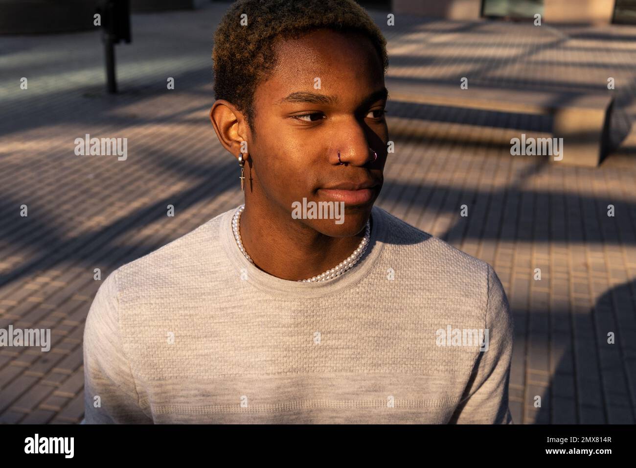 Homme afro-américain confiant dans des vêtements décontractés avec boucles d'oreilles qui regardent loin en étant debout dans la rue Banque D'Images