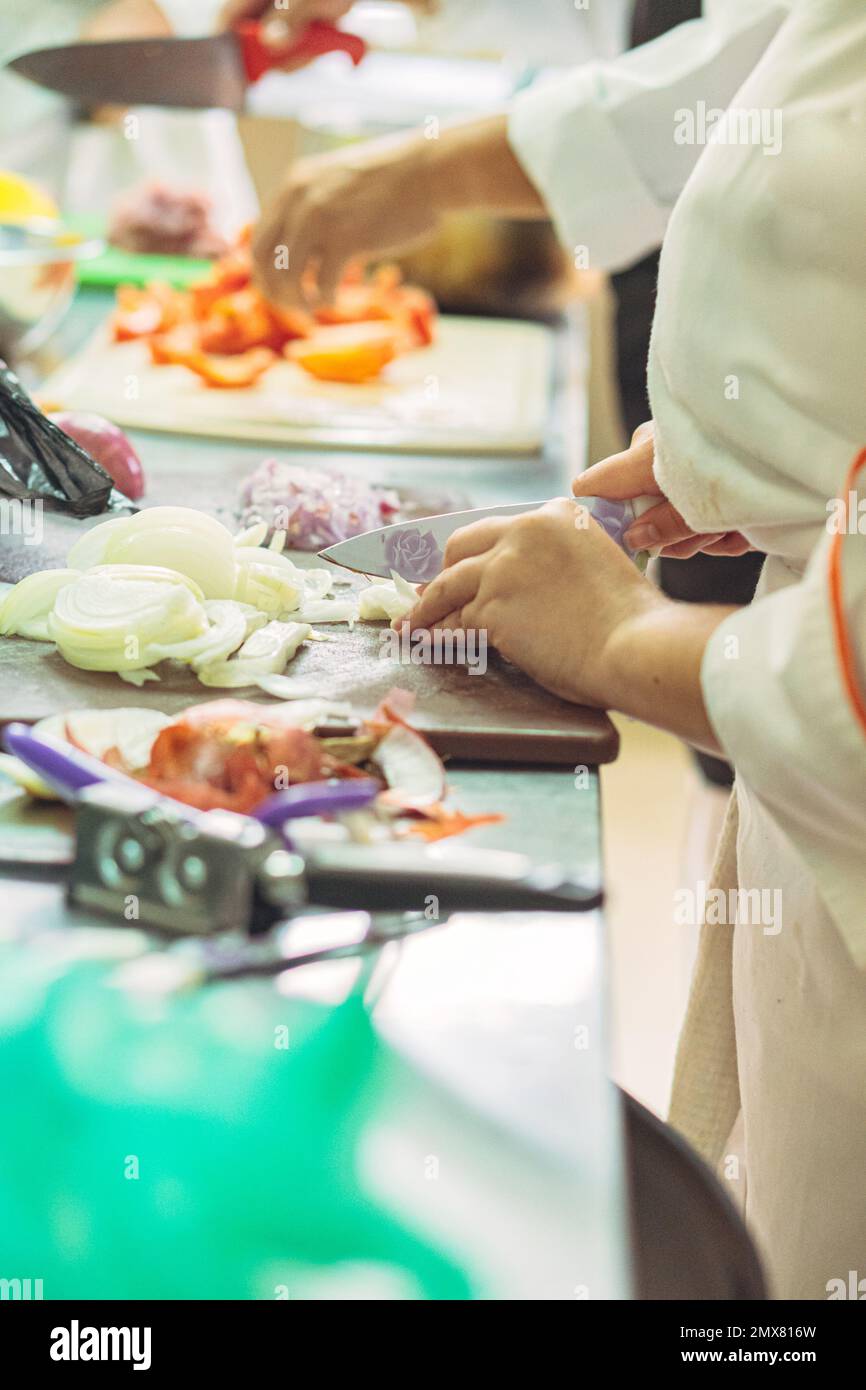 Vue latérale de la récolte anonyme femmes cuisiniers en uniforme debout au comptoir de couper les légumes tout en préparant la nourriture dans la cuisine du restaurant Banque D'Images