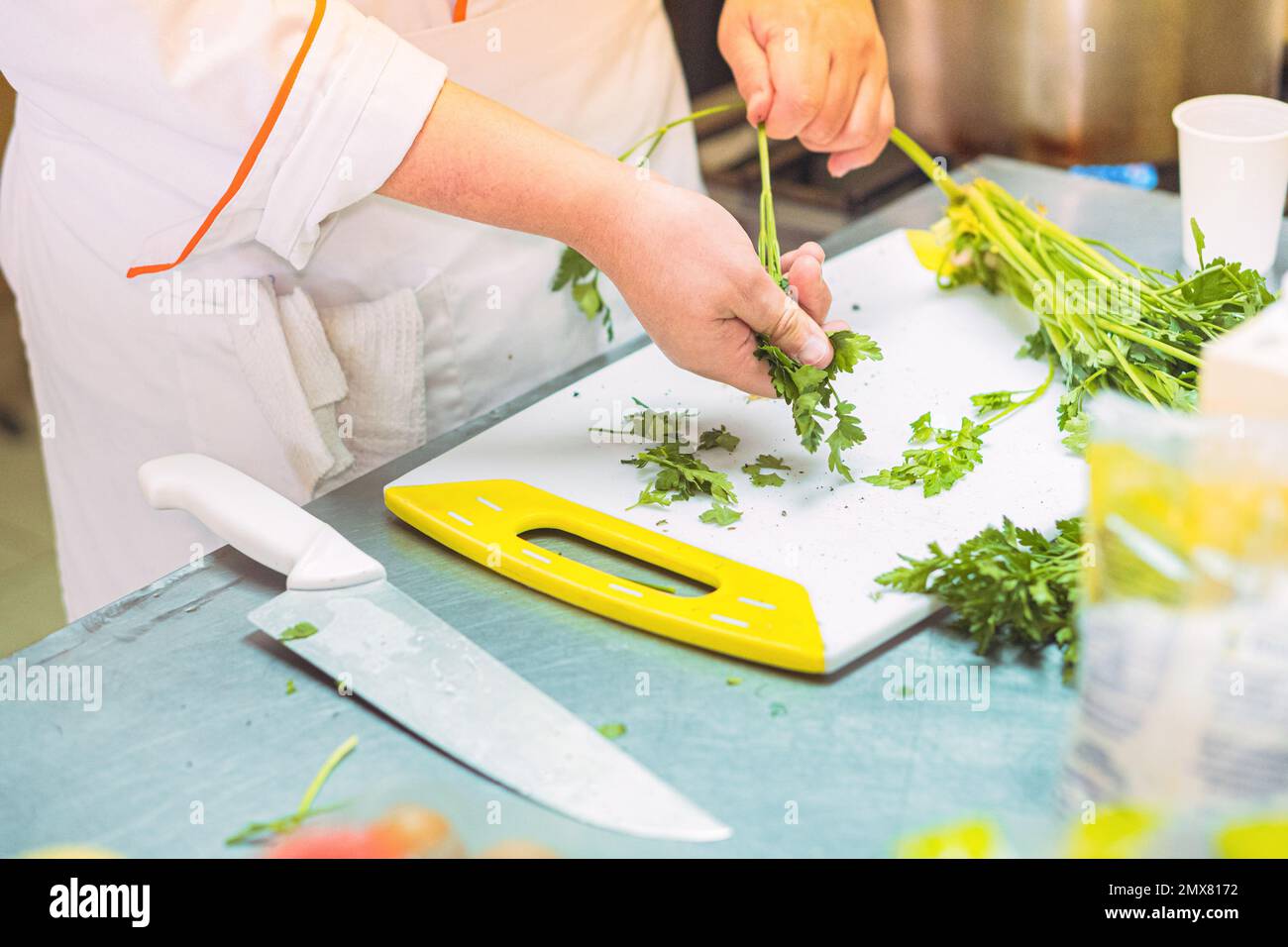 Croise le chef féminin en uniforme en enlevant les feuilles de coriandre des tiges sur la planche à découper près du couteau au comptoir dans la cuisine Banque D'Images