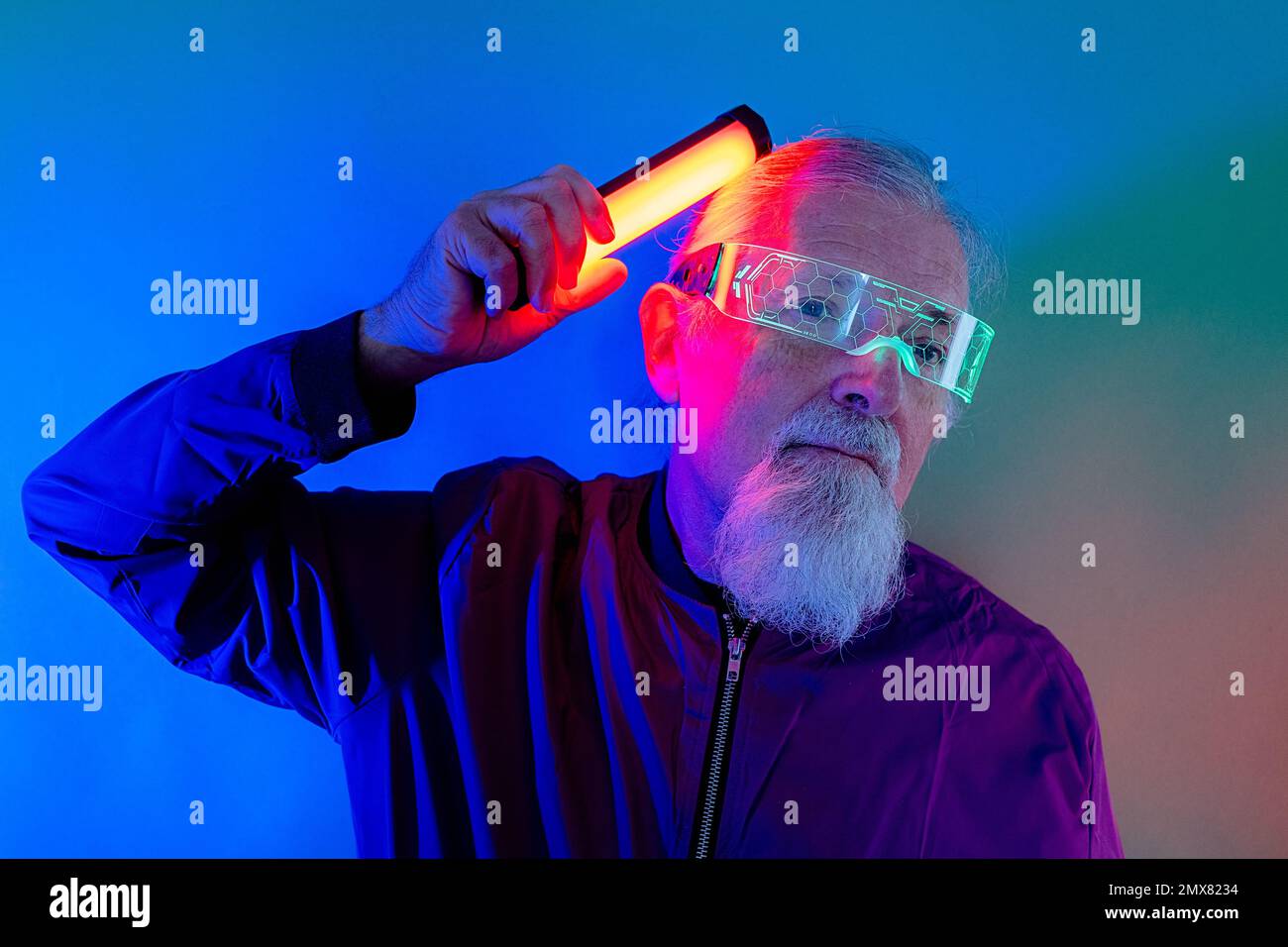 Culotte style hipster homme senior à barbe en lunettes et tenue décontractée avec vue sur le mur et lampe au néon en studio Banque D'Images
