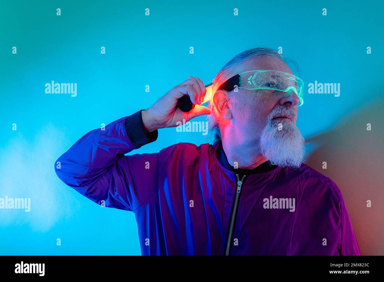 Culotte style hipster homme senior à barbe en lunettes et tenue décontractée avec vue sur le mur et lampe au néon en studio Banque D'Images