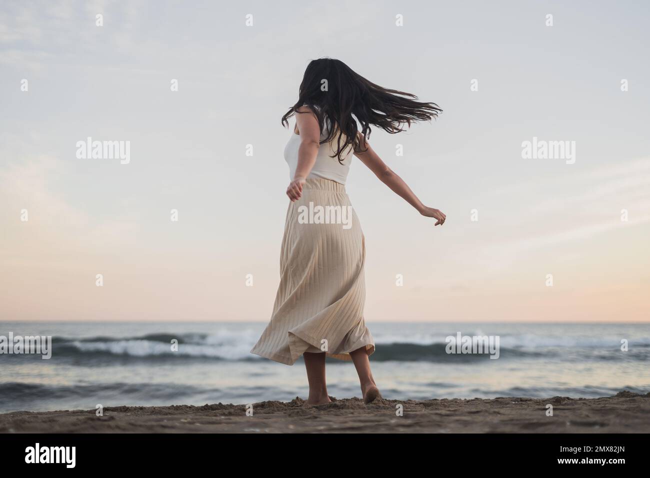 Vue arrière de jeune femme malin et méconnaissable, avec de longs cheveux sombres dans des vêtements d'été dansant sur une plage de sable, près de la poulamière Banque D'Images