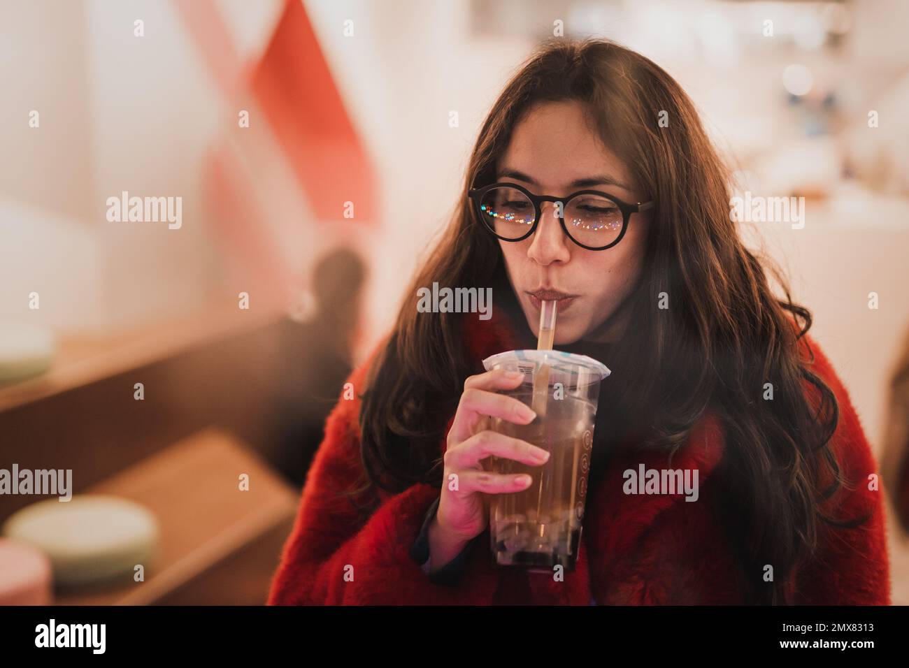 Par la fenêtre de la jeune femme réfléchie dans des vêtements chauds et des lunettes tout en ayant boire dans le café de Londres pendant le week-end Banque D'Images