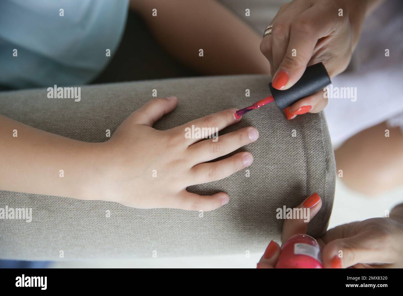 Vue de dessus de maman méconnaissable faisant manucure avec vernis à ongles rose à l'enfant tout en étant assis à la table Banque D'Images
